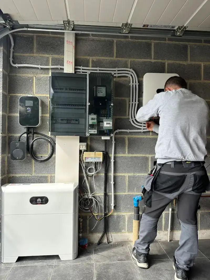 Électricien au travail dans un garage : tableau, borne de recharge et batterie domestique
